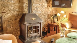 A cozy living room with a stone wall, a fireplace, a TV mounted on the wall, and a comfortable sofa.
