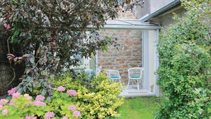 Ein kleiner Garten mit einer Steinmauer, zwei weißen Korbstühlen mit blauen Kissen und rosa Hortensienbüschen.