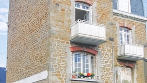 Ein mehrgeschossiges Gebäude mit Steinfassade, Balkonen mit weißen Geländern und Fensterkästen mit Blumen.