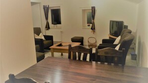 A living room with a wooden dining table, two sofas, a TV, and a window with curtains.