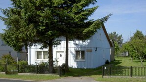 A small, white, single-story building with a sloped roof, a small porch, and a fenced yard.
