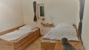 A small, clean room with two wooden beds, a wooden dresser, and a small window with curtains.