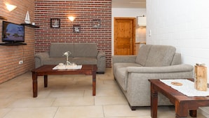 A living room with two sofas, a wooden coffee table, a TV mounted on a brick wall, and a wooden door. - Apartment 4 - Landhaus Spittdiek (Neuharlingersiel)