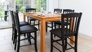 A dining area with a wooden table and black chairs, large windows, and a view of greenery outside. - Apartment 4 - Landhaus Spittdiek (Neuharlingersiel)