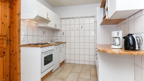 A modern kitchen with white cabinets, a wooden countertop, a stove, and a coffee maker. - Apartment 4 - Landhaus Spittdiek (Neuharlingersiel)