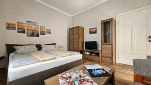 Ett hotellrum med en säng, en tv, en garderob i trä, ett skrivbord med ett glas på och en dörr.