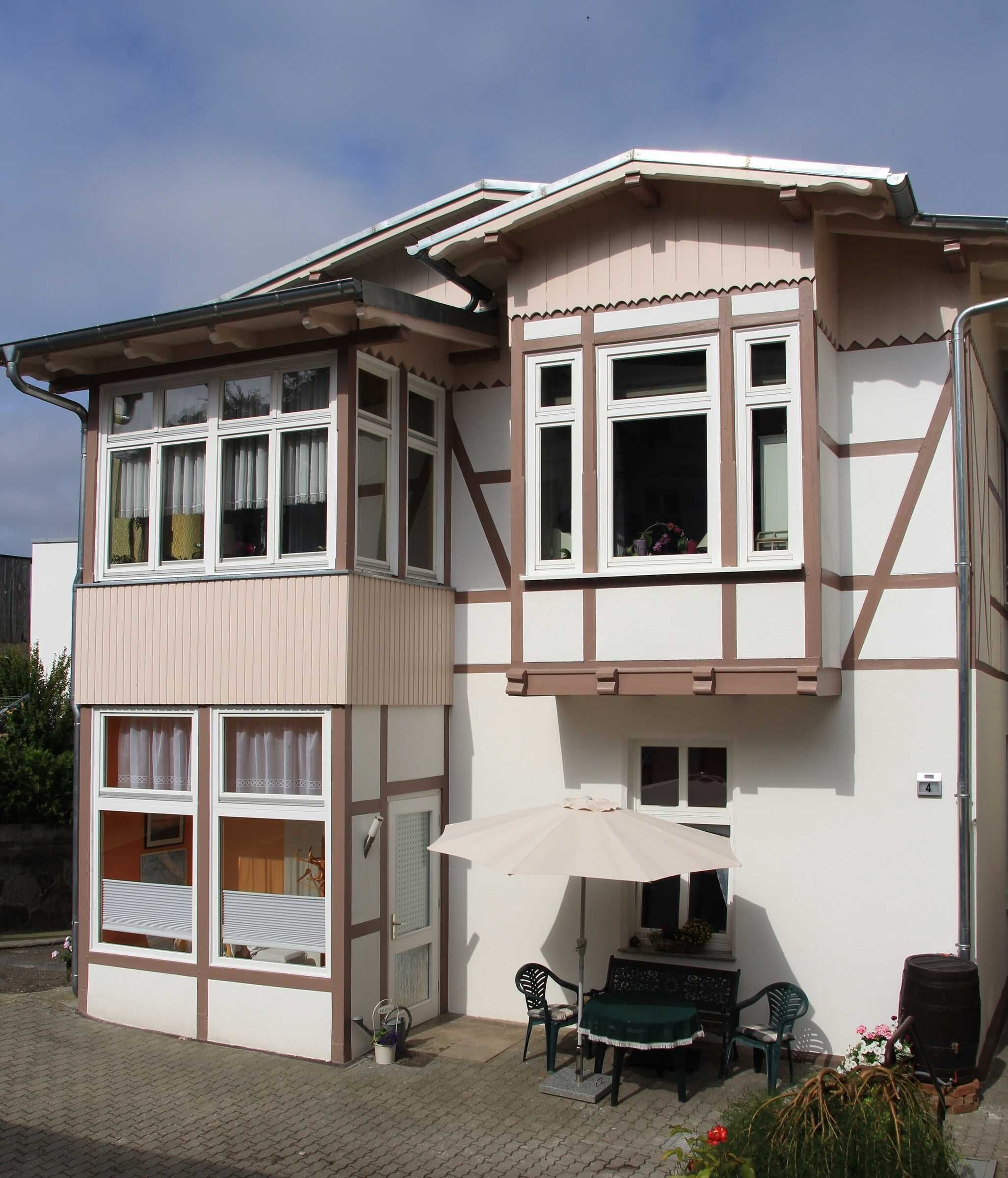 Un bâtiment à deux étages doté d’un balcon, d’une fenêtre avec des rideaux et d’un petit espace extérieur aménagé avec une table et des chaises.
