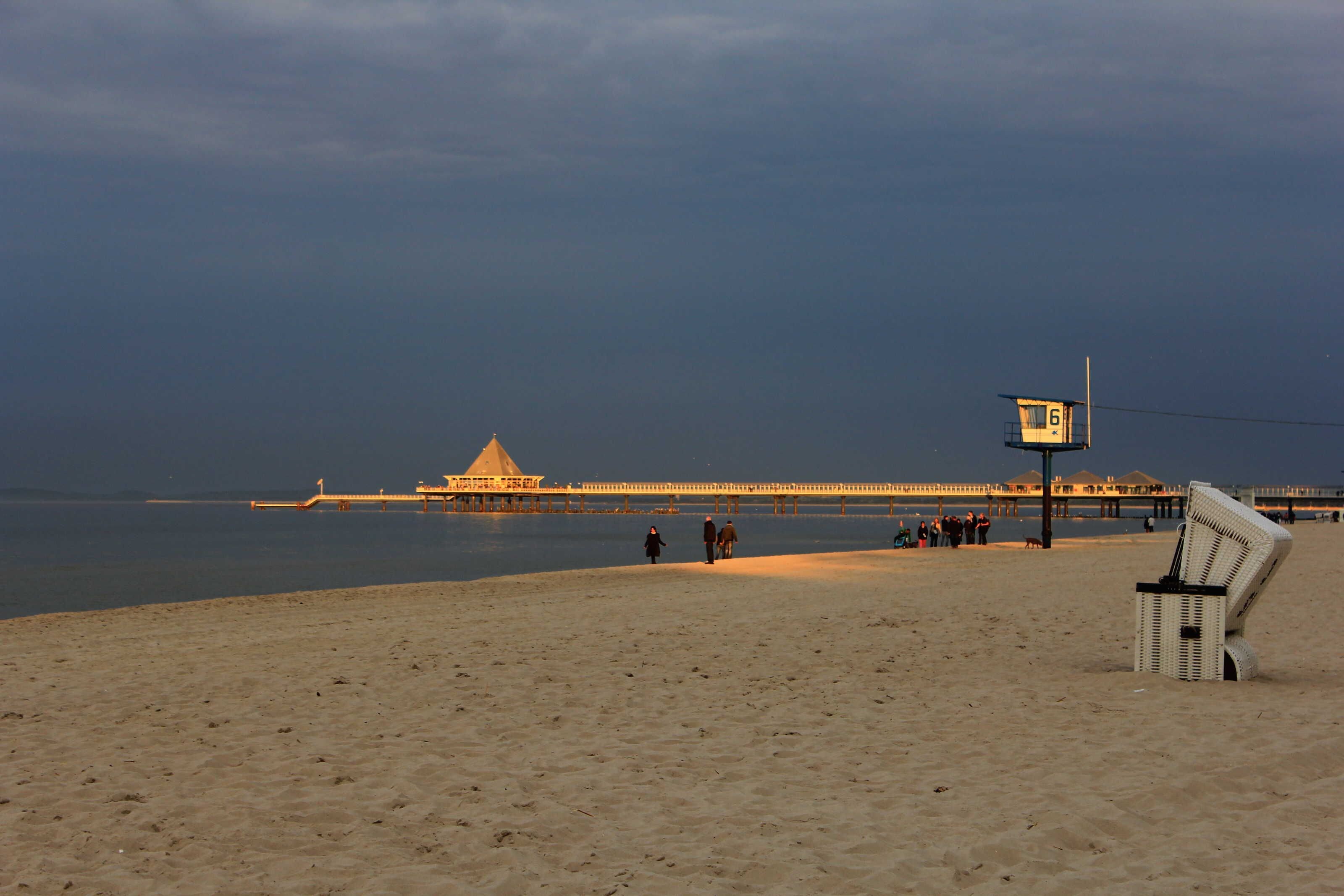 Een strand met een steiger, een redershut en een stoel.