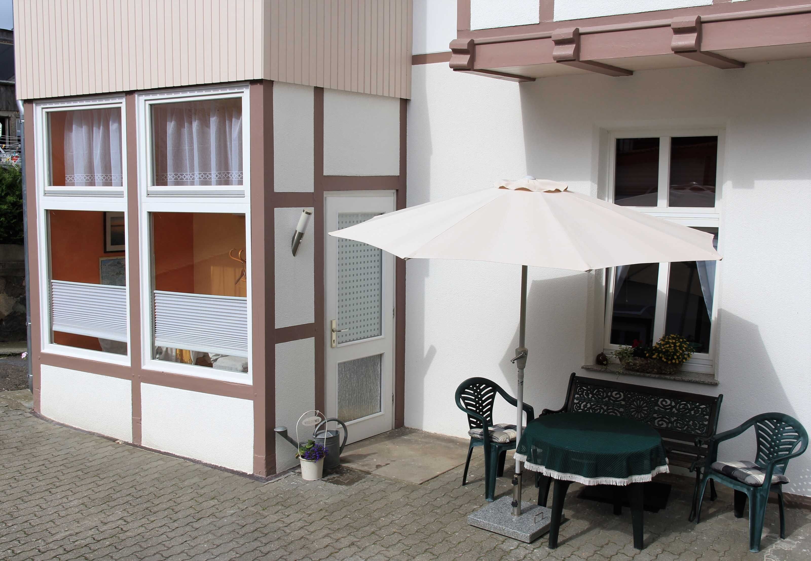 Een terras met een tafel, stoelen, een parasol en een raam met een bloembak.