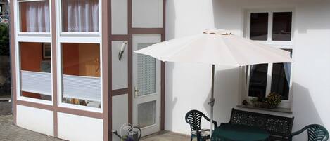 Een terras met een tafel, stoelen, een parasol en een raam met een bloembak.