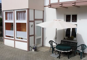 A patio area with a table, chairs, an umbrella, and a window with a flower box. - Vacation apartment - Bungalow & vacation apartment Fuchs (Heringsdorf)