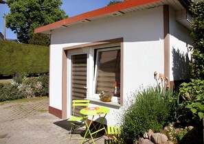 Une petite maison avec un patio, une porte-fenêtre coulissante, une chaise jaune et une petite table.