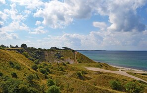 A coastal landscape with a dirt path leading to a beach, surrounded by grassy hills and sparse trees. - 4 bedroom cozy home in Nykøbing Sj (Nykøbing Sj)