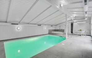 Une piscine intérieure à l’eau légèrement verdâtre, avec des murs blancs et un sol carrelé.