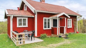 Una casa de madera roja con techo de tejas, un porche con sillas y una mesa, y un pequeño jardín.