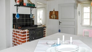 Una cocina con horno de ladrillo, una mesa blanca con platos y velas, y una puerta con picaporte decorativo.