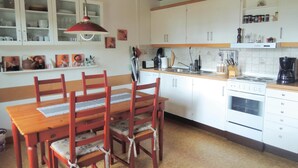 Una cucina con mobili bianchi, un tavolo da pranzo in legno con sedie, una lampada a sospensione rossa e una macchina da caffè.