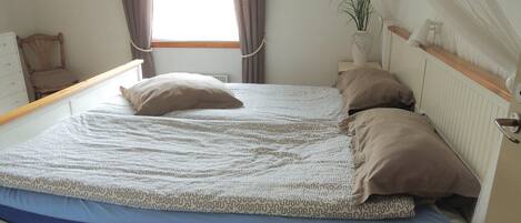 Una cama con ropa de cama estampada, una mesita de noche con lámpara y una ventana con cortinas.
