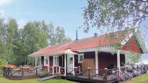 Una baita in legno con tetto rosso, un portico con ringhiere in legno e una piccola terrazza con posti a sedere esterni.
