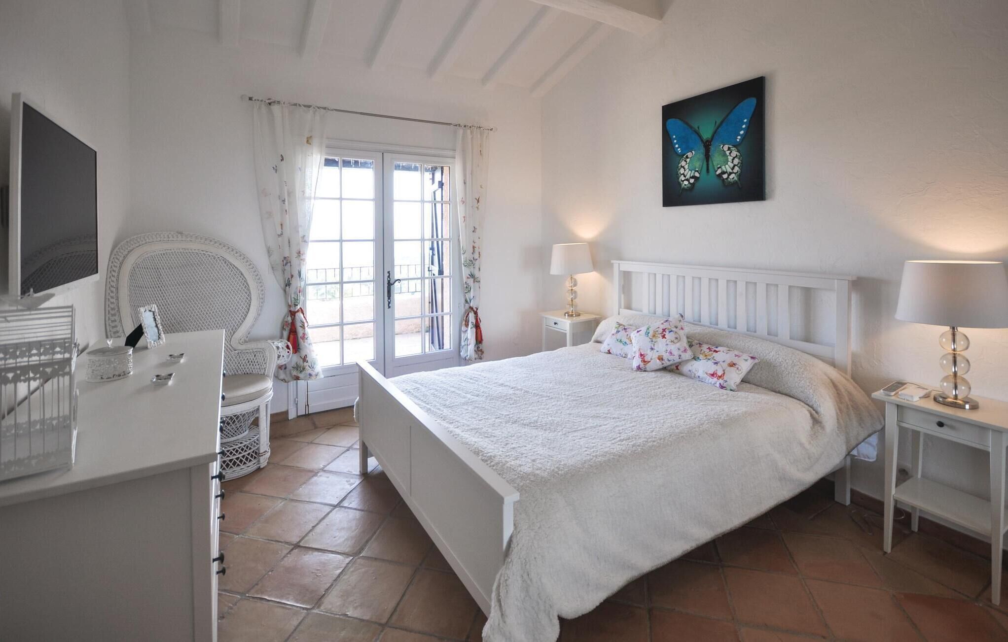 A bedroom with a large bed, a chair, a desk, and a window with curtains.