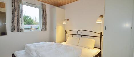 Een slaapkamer met een bed, houten plafond, twee wandlampen en een raam met gordijnen.