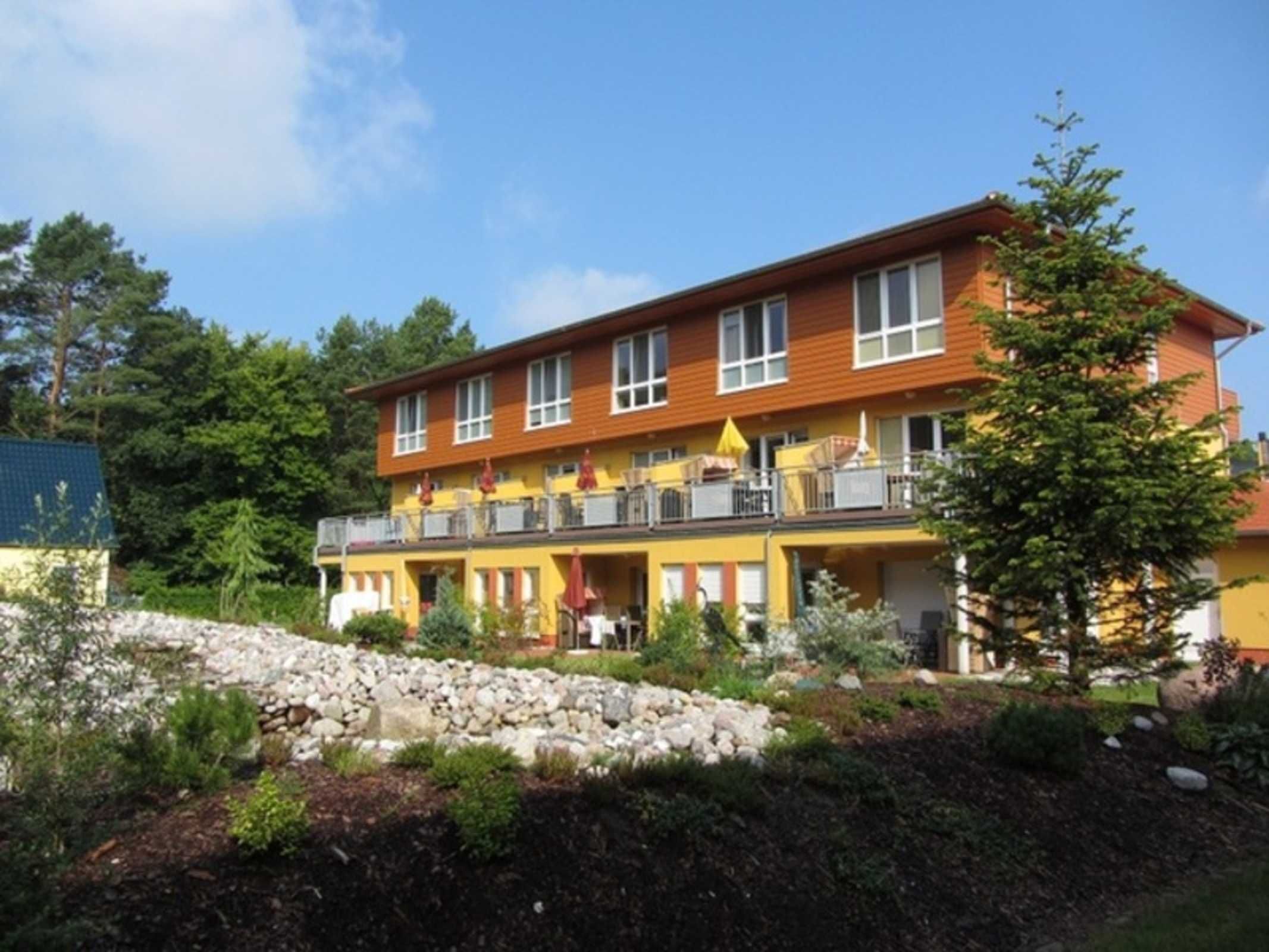 Un hotel de varios pisos con balcones, un muro de piedra y un jardín ajardinado.