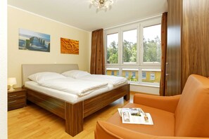 Une chambre à coucher avec un lit, une table de chevet, une fenêtre avec des rideaux et une vue sur les bâtiments à l’extérieur.