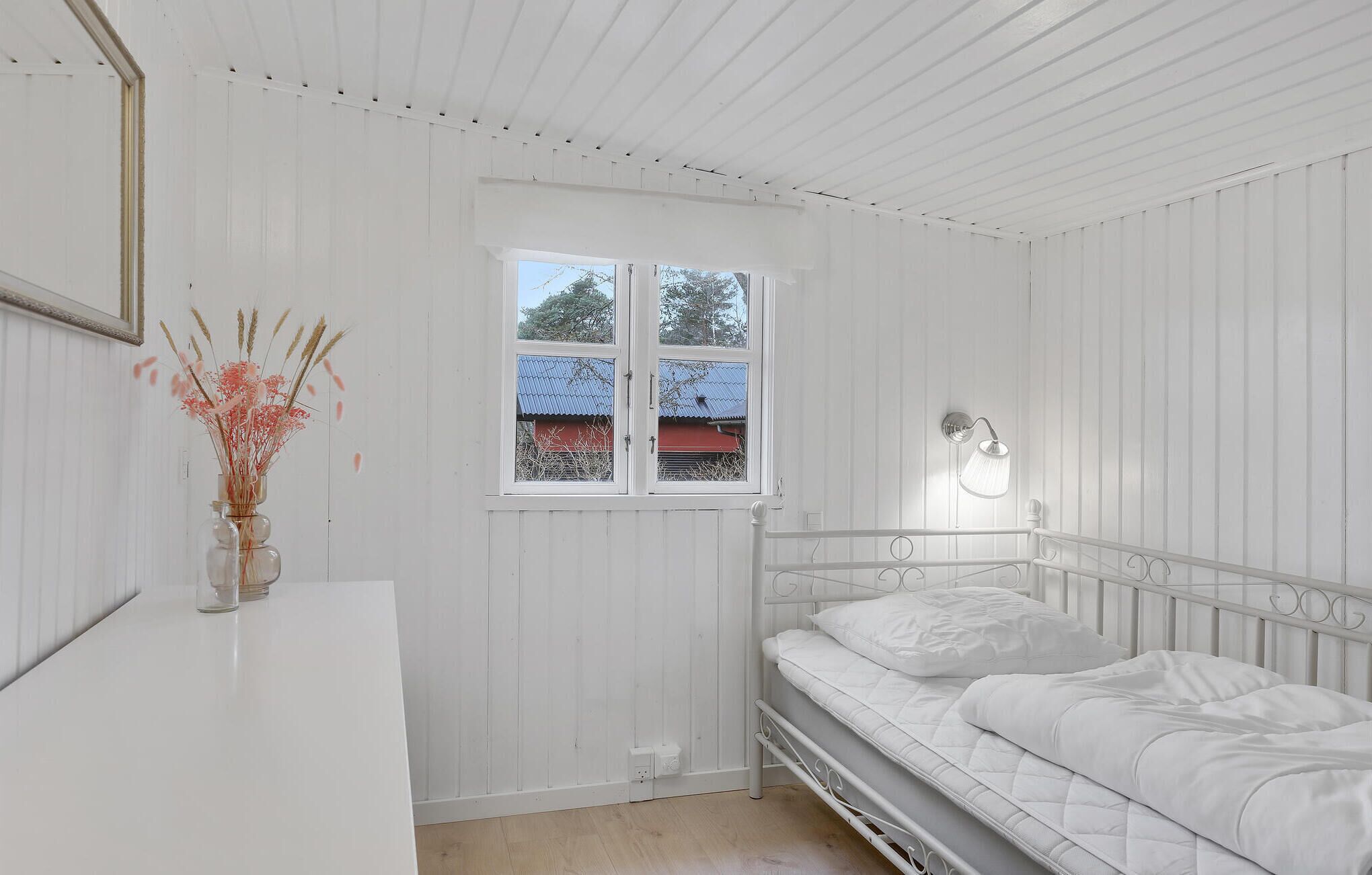 Una habitación blanca con una cama, una ventana y un florero con flores.