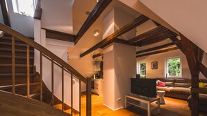 Een ruime loft met een houten trap, een zithoek met een bank en televisie, en een keuken op de achtergrond.