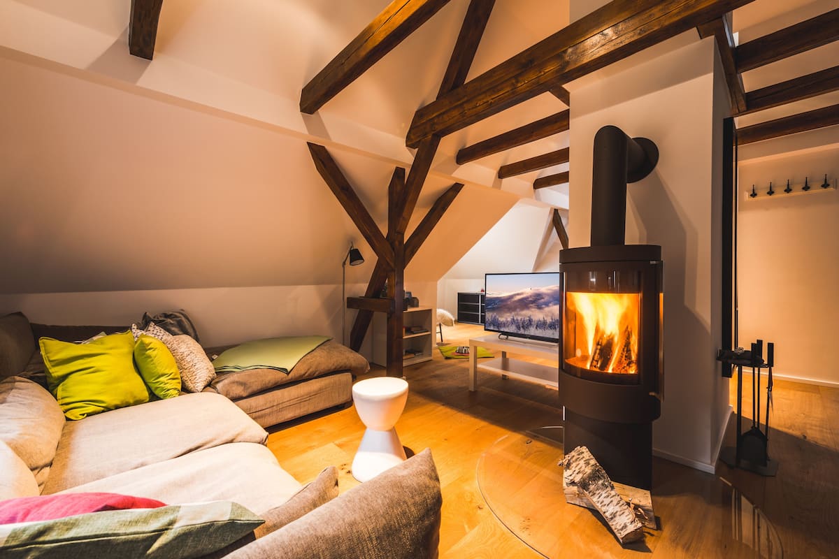 A cozy loft bedroom with a wooden ceiling, a large TV, and a fireplace.