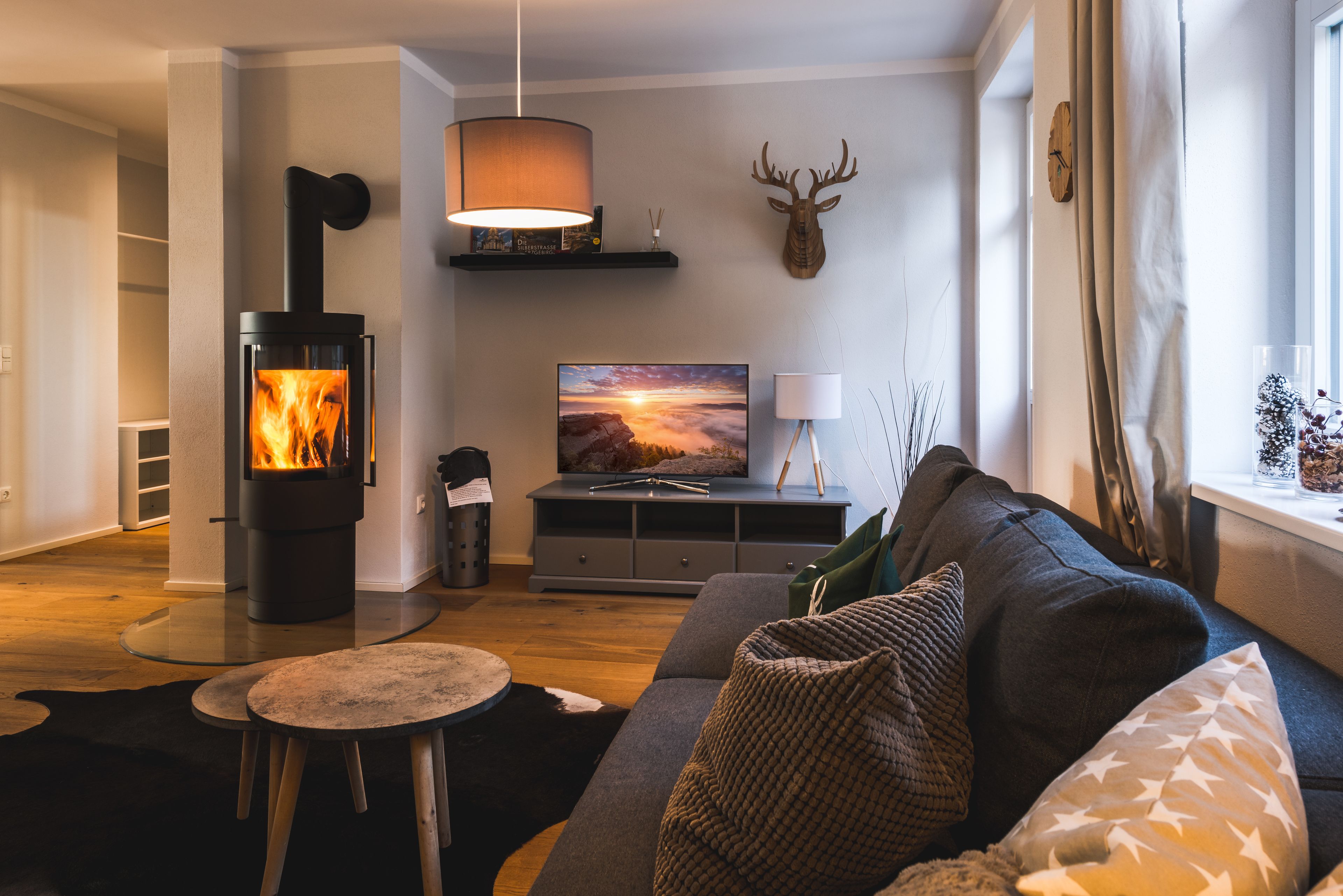 Ein gemütliches Wohnzimmer mit Kaminofen, einer bequemen Couch, einem kleinen runden Tisch und einem Fernseher auf einem Schrank.