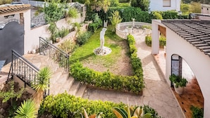 A garden with a central statue, stone steps, and a white building in the background.