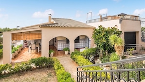 A Mediterranean-style villa with a covered patio, tiled roof, and a garden with various plants.