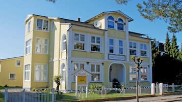 Ein zweistöckiges Gebäude mit gelber Fassade, zahlreichen Fenstern und einem Schild, das es als Villa kennzeichnet.