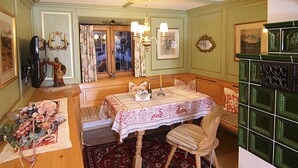 Una habitación con una mesa de madera dispuesta para dos personas, una silla, un tapete estampado y un mueble verde con azulejos decorativos.