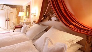Habitación de hotel con dos camas, un cabecero decorado, un escritorio con lámpara y una silla.