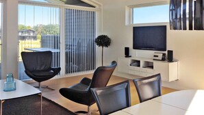 A modern living room with a flat-screen TV, a dining table, and two black chairs.