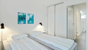A bedroom with a bed, two wall-mounted abstract paintings, a bedside lamp, and a white wardrobe.