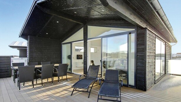 A modern outdoor deck with a glass enclosure, wooden flooring, and metal chairs.