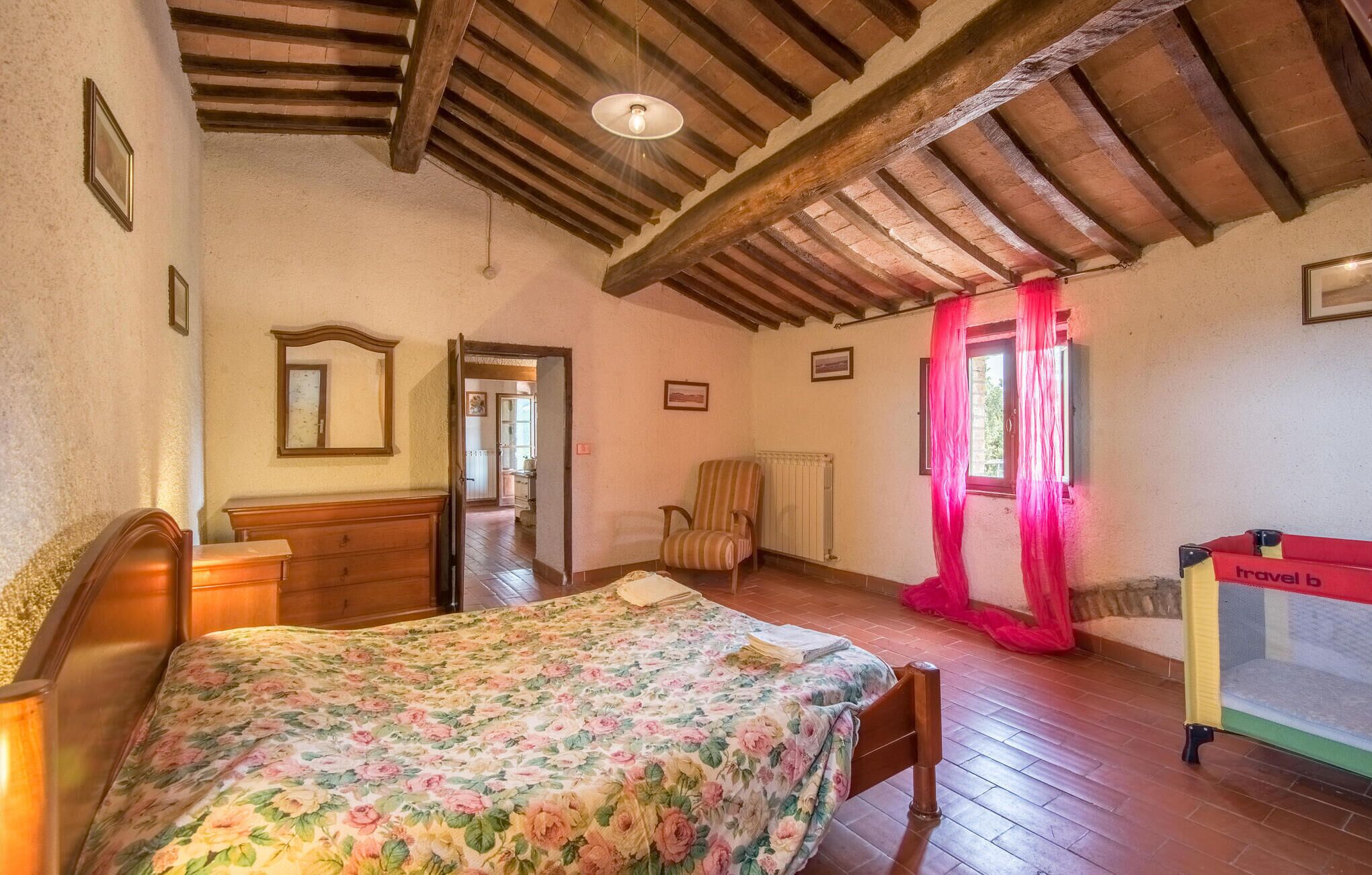 Een slaapkamer met een houten bed, een stoel, een radiator en een raam met gordijnen.