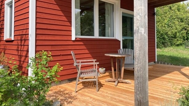 A red wooden house with a porch, a wooden bench, and a small table.