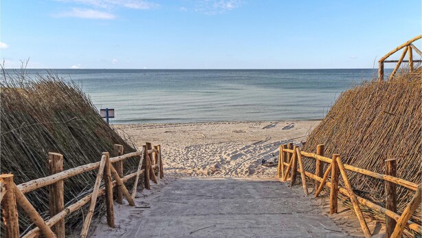 Een strandpad dat naar de zee leidt, met rieten gebouwen aan beide zijden.