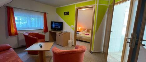 Une chambre d’hôtel de taille réduite, équipée d’une télévision, d’un petit bureau, d’un canapé et d’un lit.