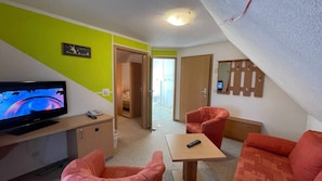 A room with a television, a small table, two chairs, a mirror, and a door leading to a bathroom.