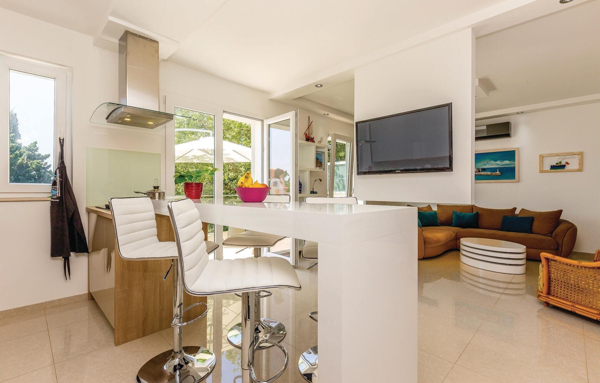 Una cocina moderna con una isla central, taburetes de bar y una zona de comedor con sofá y mesa baja.