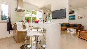 Una cucina moderna con isola centrale, sgabelli da bar e zona pranzo con divano e tavolino.