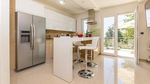 Una cucina moderna con frigorifero integrato, un'isola centrale con sgabelli da bar e un'ampia porta scorrevole in vetro che dà su un balcone.