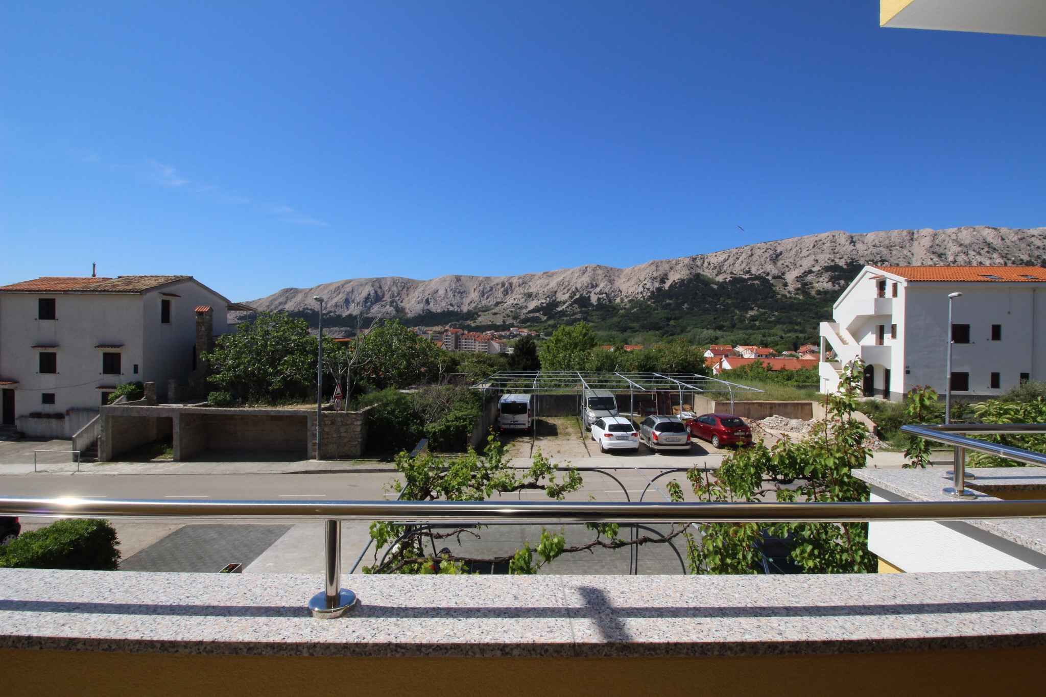 A view of a parking area with several cars, a building with a red roof, and a mountain in the background.