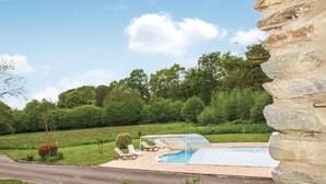 A swimming pool with a glass enclosure, surrounded by a stone wall, with a lawn and trees in the background. - Beautiful home in St Martin des Pres (St Martin des Pres)
