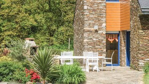 A stone building with a wooden slatted wall, a stone staircase, and a white outdoor seating area with chairs and a table. - Beautiful home in St Martin des Pres (St Martin des Pres)